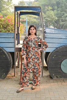 Woman in a floral jumpsuit standing in front of a blue truck with greenery in the background