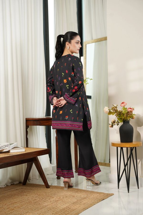 Woman wearing a black floral patterned outfit in a room with white curtains and a vase of flowers.