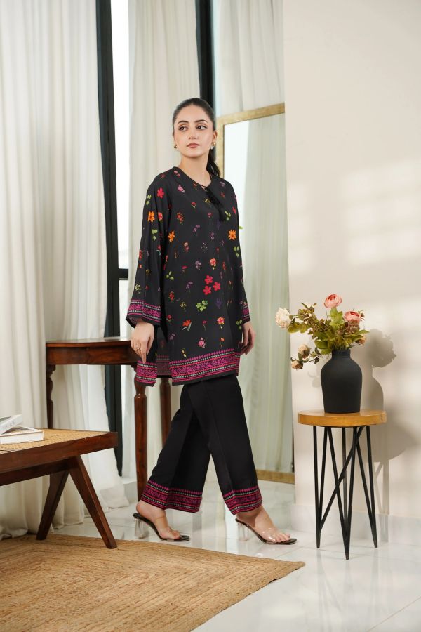 Woman wearing a dark floral outfit in a room with white walls and a wooden table.