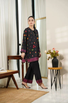 Woman wearing a dark floral outfit in a room with white walls and a wooden table.