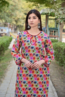 Woman wearing a colorful floral dress standing outdoors with greenery in the background