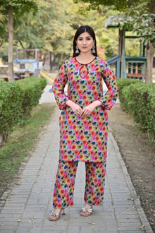 Woman in a colorful floral outfit standing on a pathway with greenery in the background