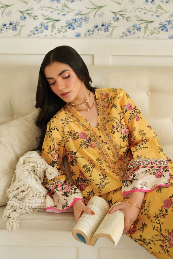 Woman in a yellow floral dress reading a book on a couch with floral wallpaper.