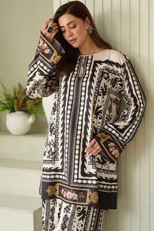 Woman wearing a black and white patterned outfit leaning against a white wall.