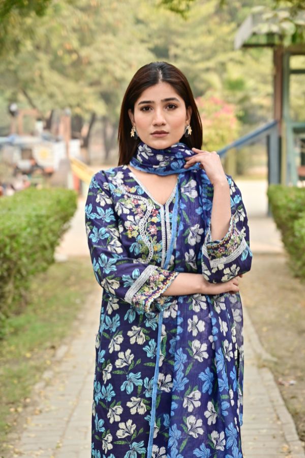 Woman wearing a blue floral dress outdoors on a path with greenery.