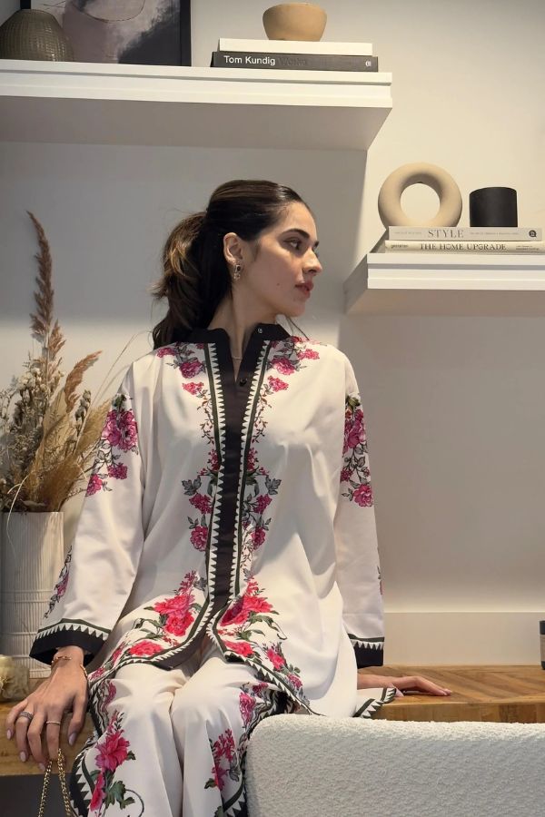 Woman wearing a white embroidered outfit sitting on a couch in a room with shelves and decor.