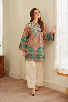 Woman wearing a colorful embroidered kurta with white pants in a room.