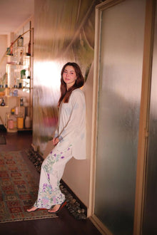 Woman in a floral outfit standing in a room with shelves and a rug.