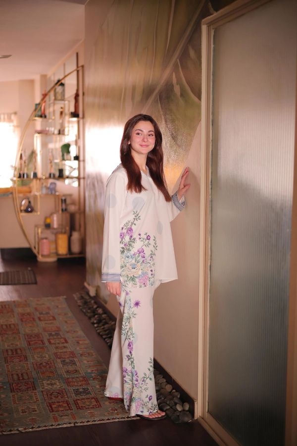 Woman in a floral dress standing in a room with a decorative wall.