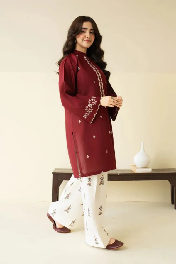 Woman wearing a maroon and white embroidered outfit standing indoors.