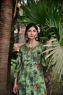 Woman in a green floral dress standing among palm leaves