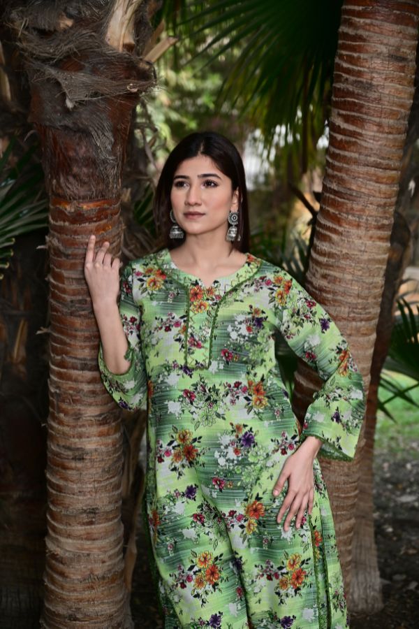 Woman in a green floral dress standing between two palm trees.