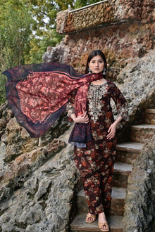 Woman in a floral outfit holding a large scarf on stone steps with greenery in the background