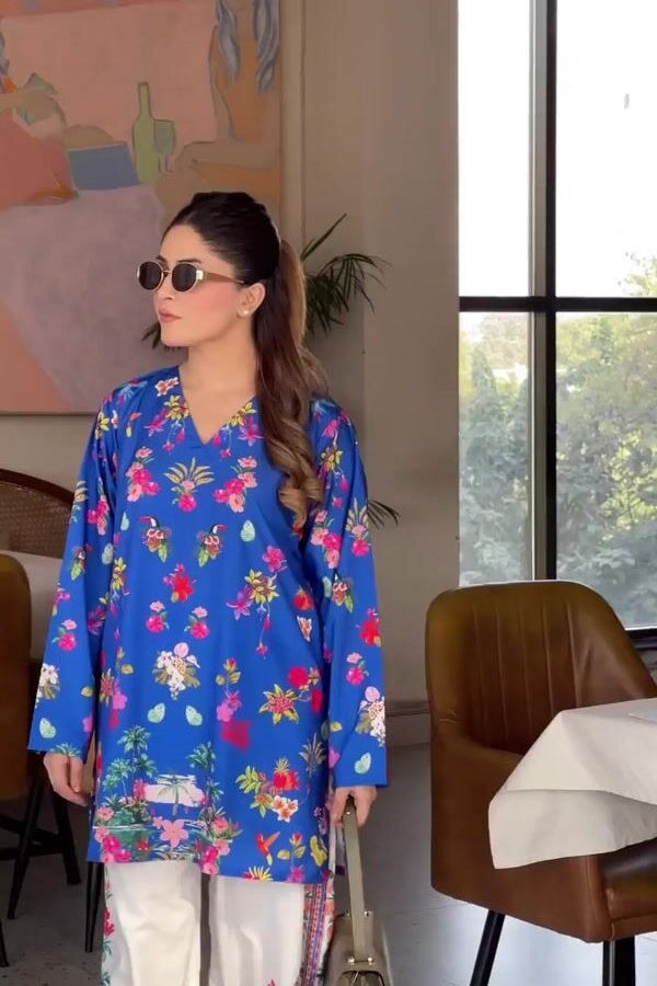 Woman in a blue floral dress standing indoors with a painting and chair in the background
