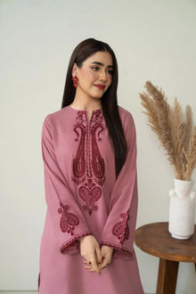 Woman wearing a pink embroidered dress standing indoors with a neutral background