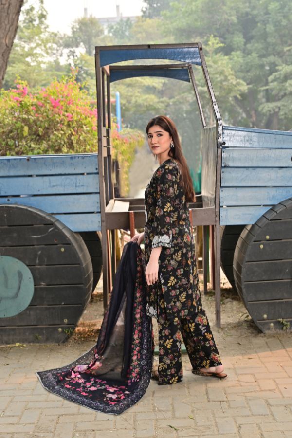 Woman in a floral dress standing in front of a wooden structure with greenery in the background