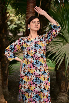 Woman wearing a colorful floral dress standing outdoors with greenery in the background